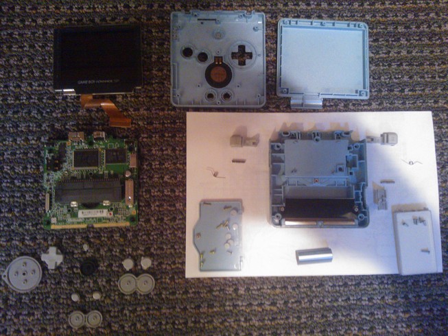 A completely disassembled Gameboy Advance SP with all of the parts
				laid out